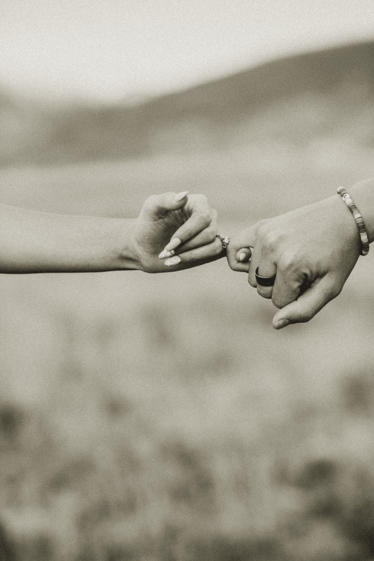 Two hands reaching towards each other with intertwined pinky fingers against a blurred background.