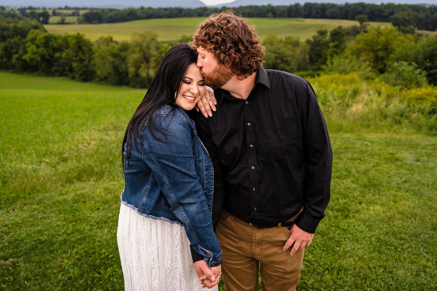 A couple shares intimate moments in a lush green countryside setting.