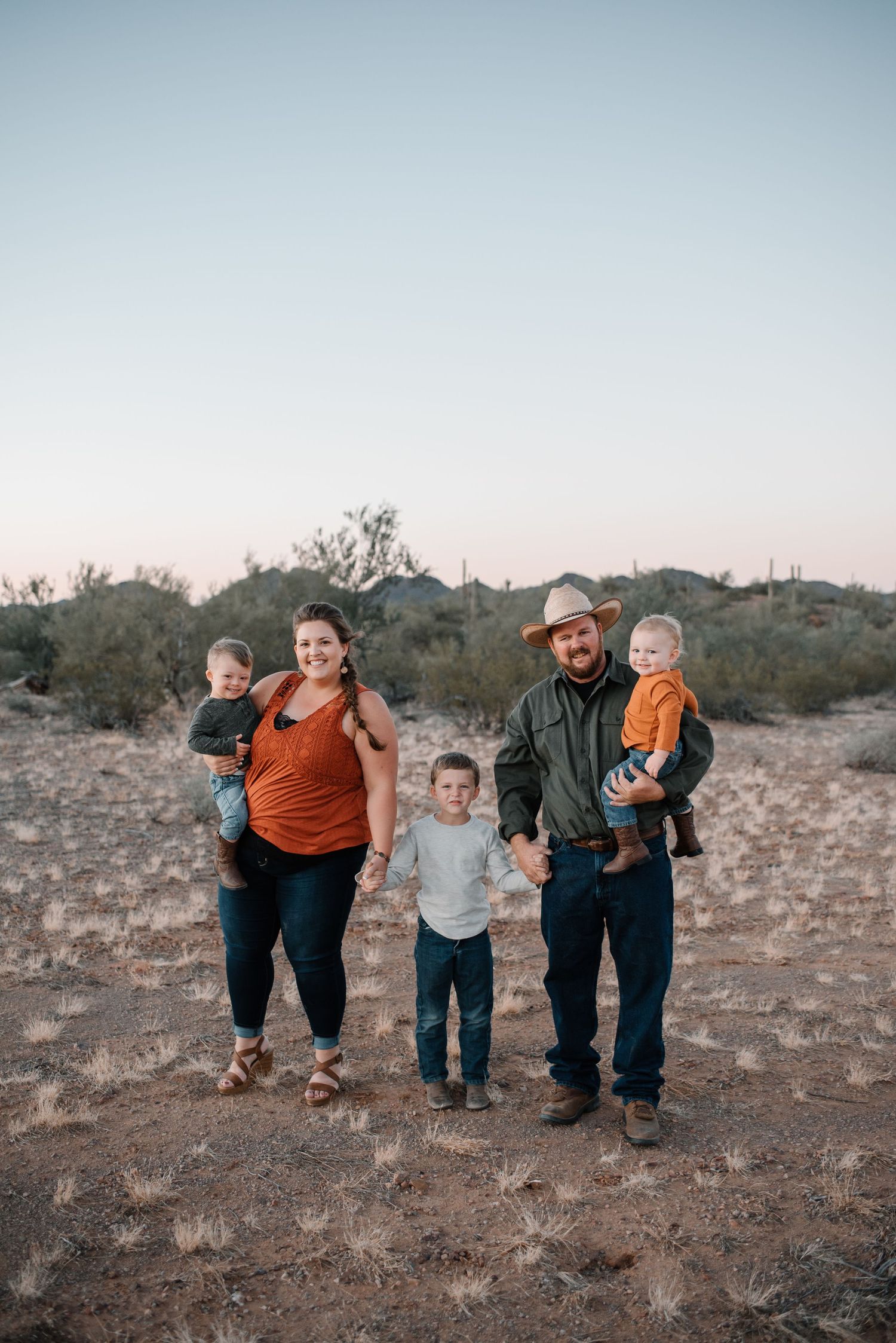Family playfully poses together in desert landscape at sunset.