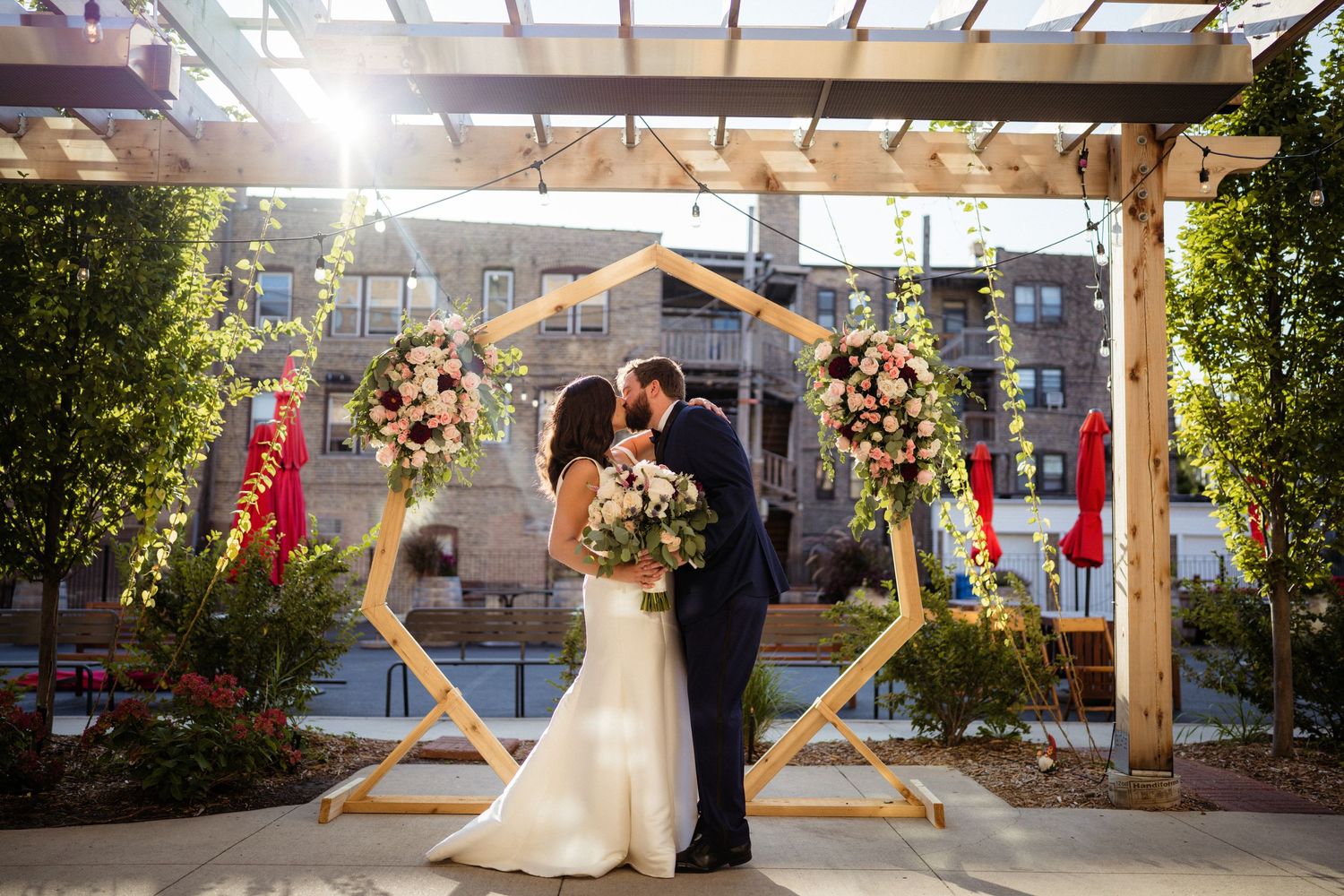 Romantic wedding ceremony under a wooden pergola decorated with floral arrangements and a geometric arch.
