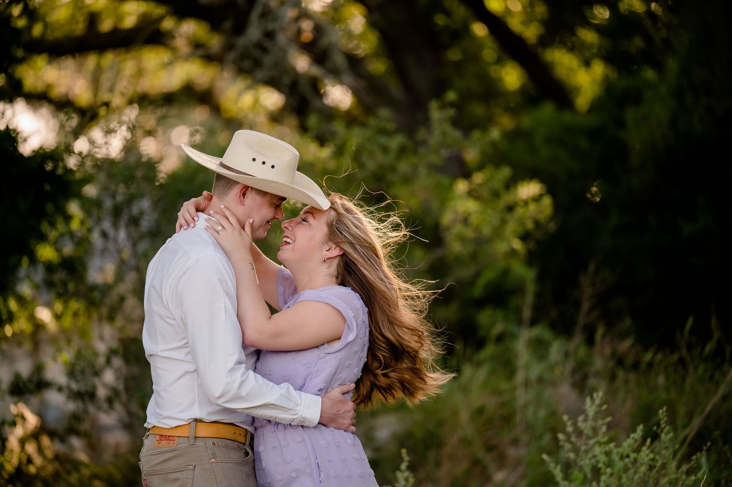 Romantic couple embracing in field during golden hour with cowboy hat.