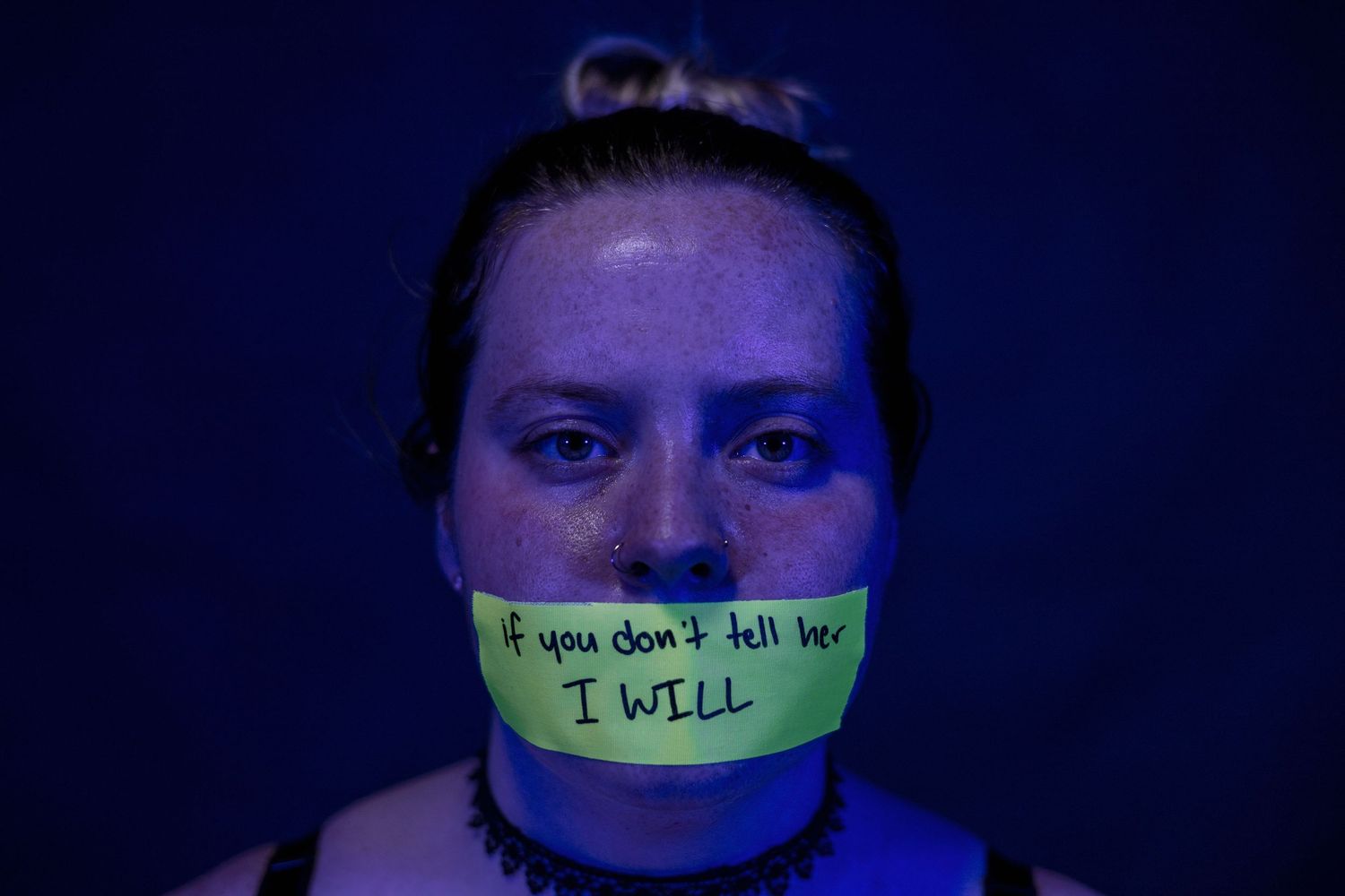 Person illuminated in blue light with tape across their mouth.