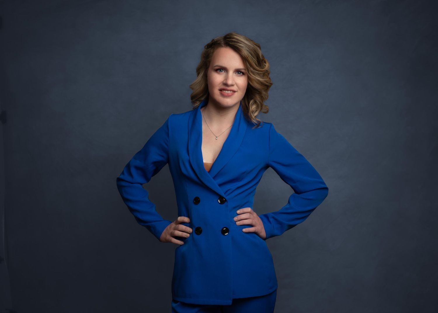jonge vrouw in blauw pak, krachtig met armen in haar zijde geposeerd