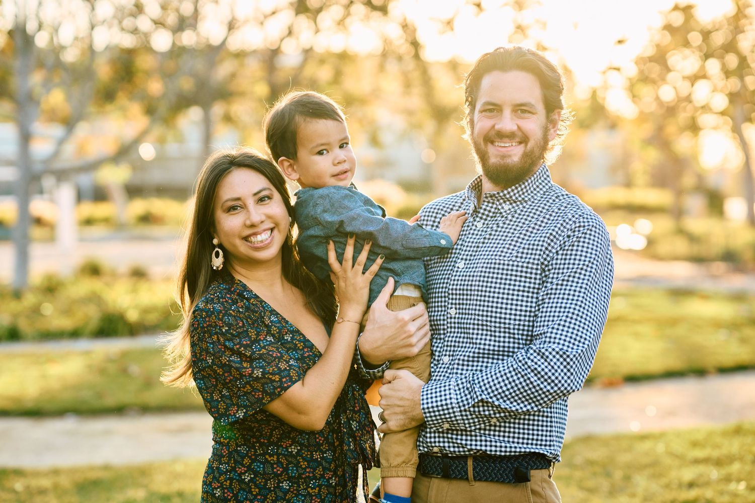 Family portrait in a park during golden hour with autumn trees in background.