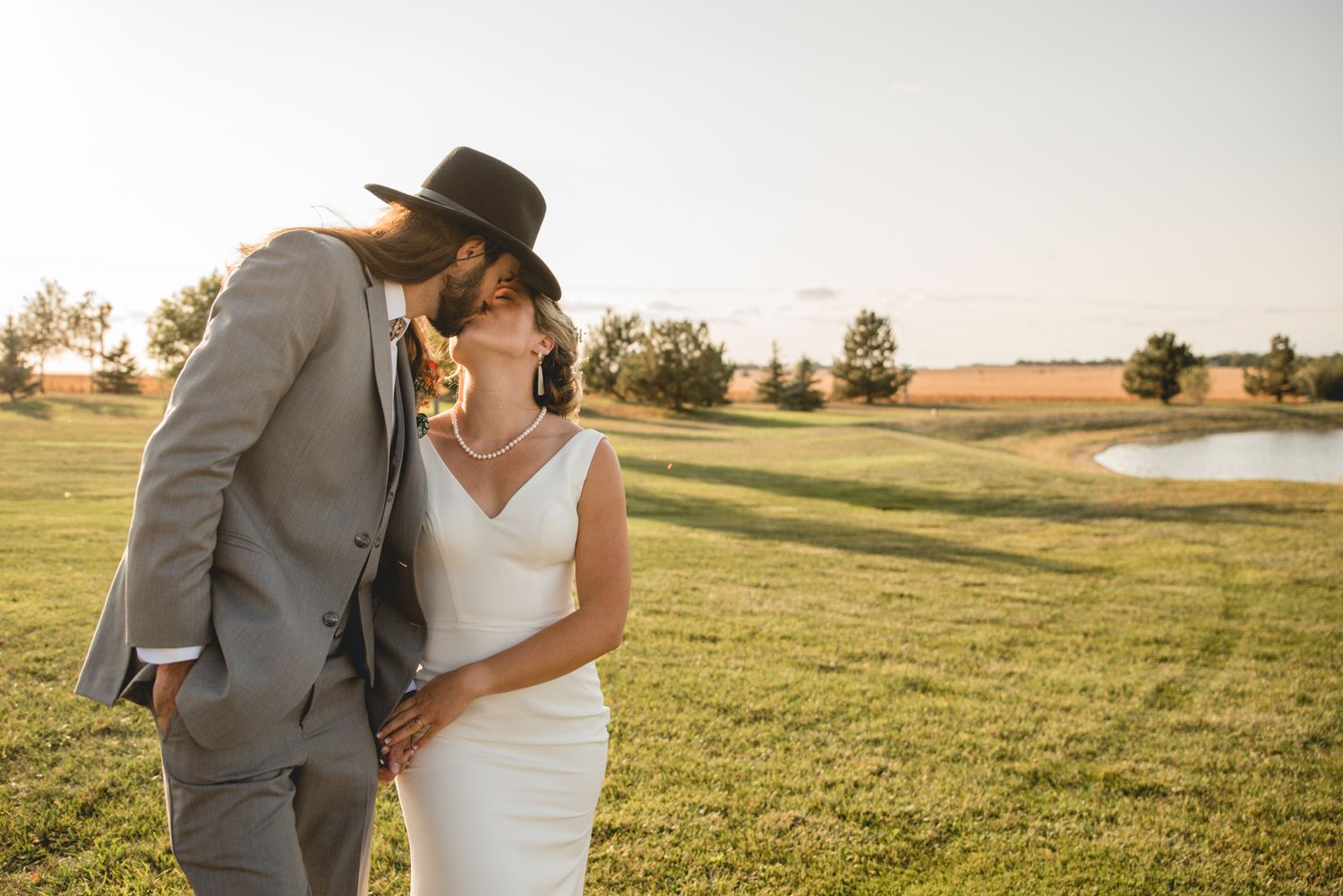Sunset wedding portrait in an outdoor field setting with a pond in the background.