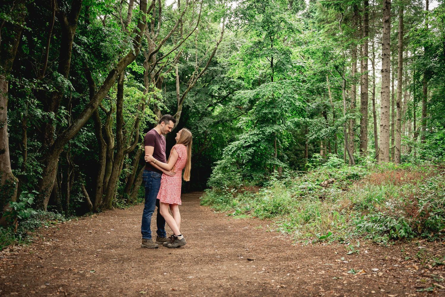 A couple walks hand in hand through a lush wooded forest path.