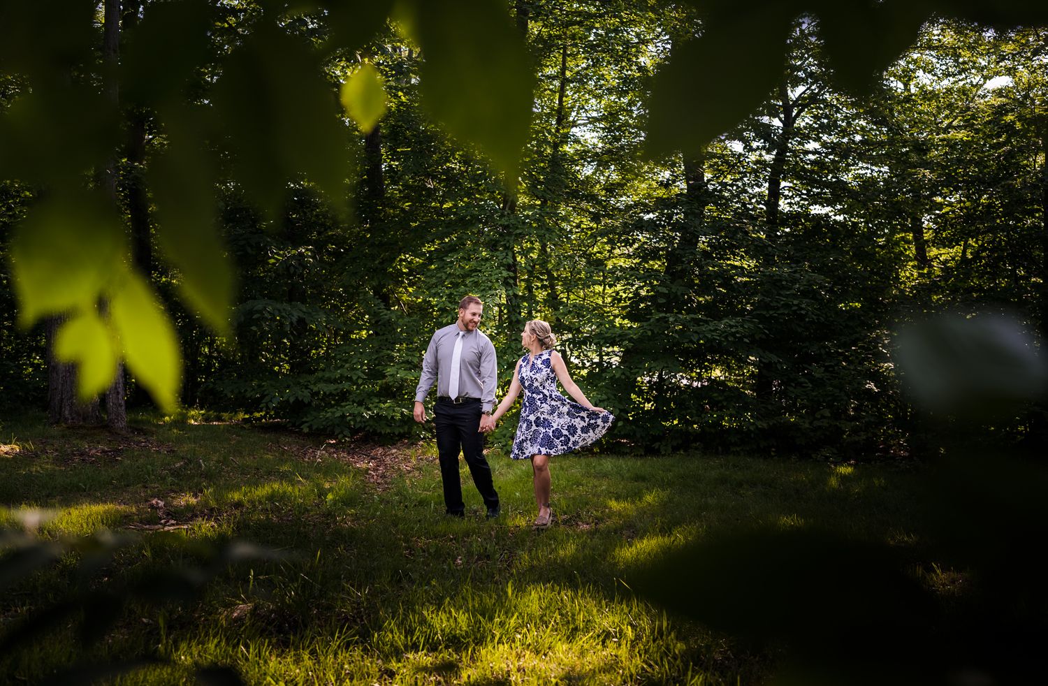 Sunlit forest engagement session with golden light filtering through leaves.