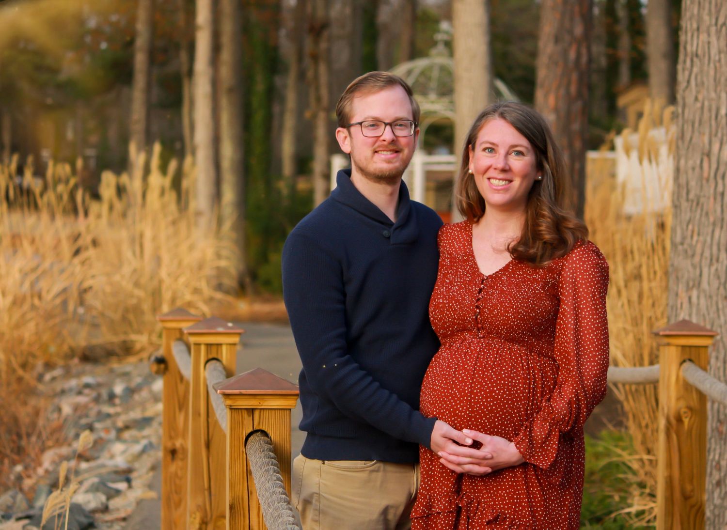 A couple poses together on a wooden bridge during golden hour with fall foliage in the background.