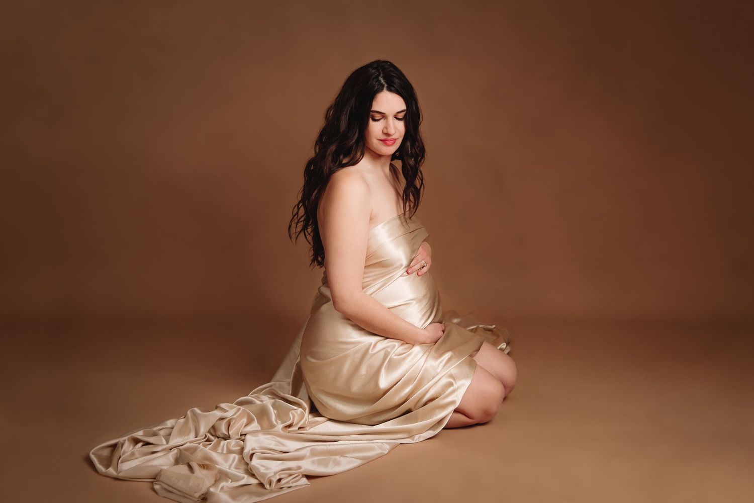 pregnant woman kneeling and draped in gold fabric by kansas city maternity and newborn photographer