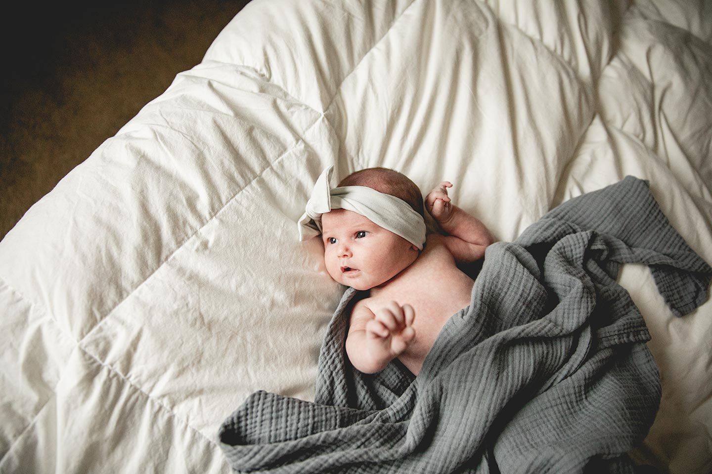 newborn girl laying on bed, looking towards the window light