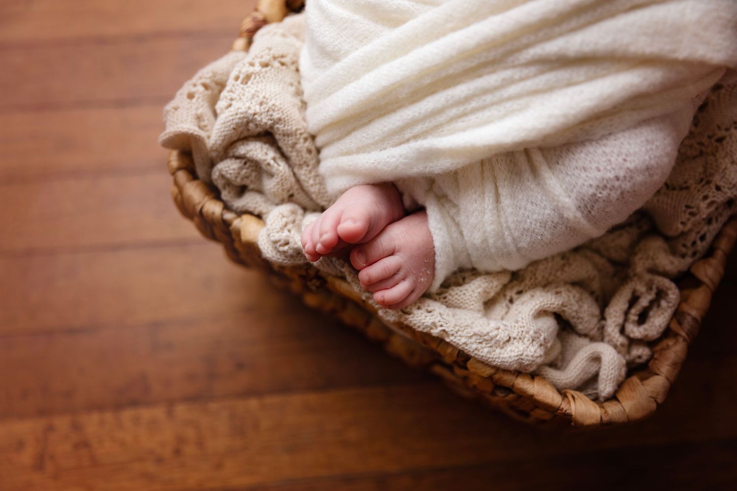 Tiny feet peeking out from white swaddle wrap on textured brown blanket.