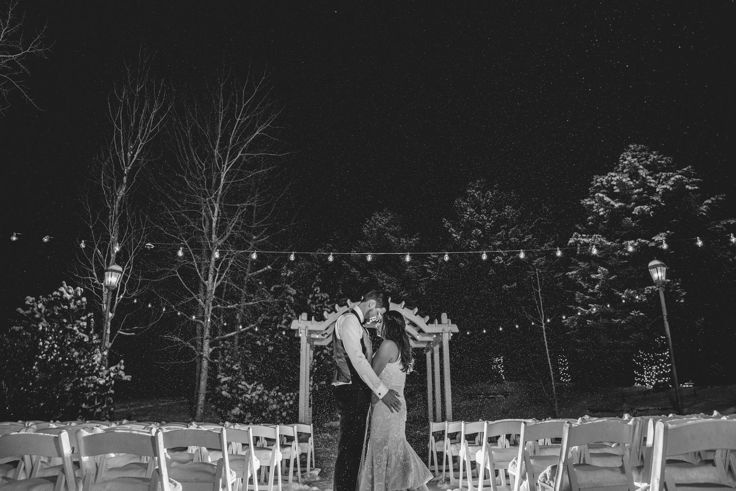 Black and white nighttime wedding portrait under string lights.