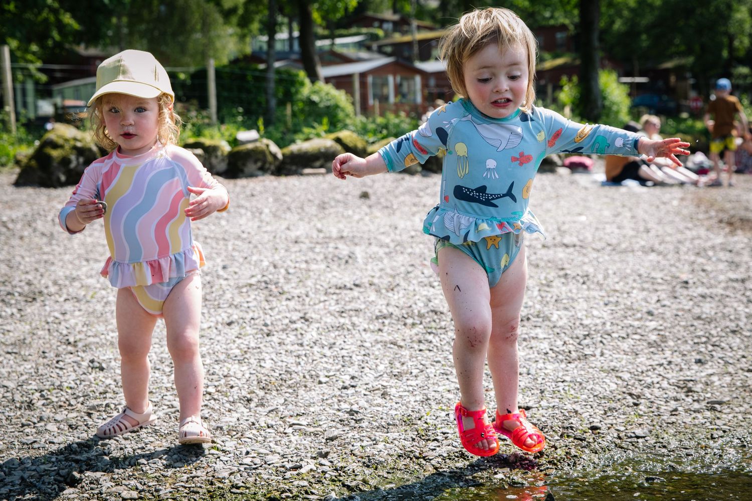 Two small children in swimsuits play on a rocky beach on a sunny summer day.