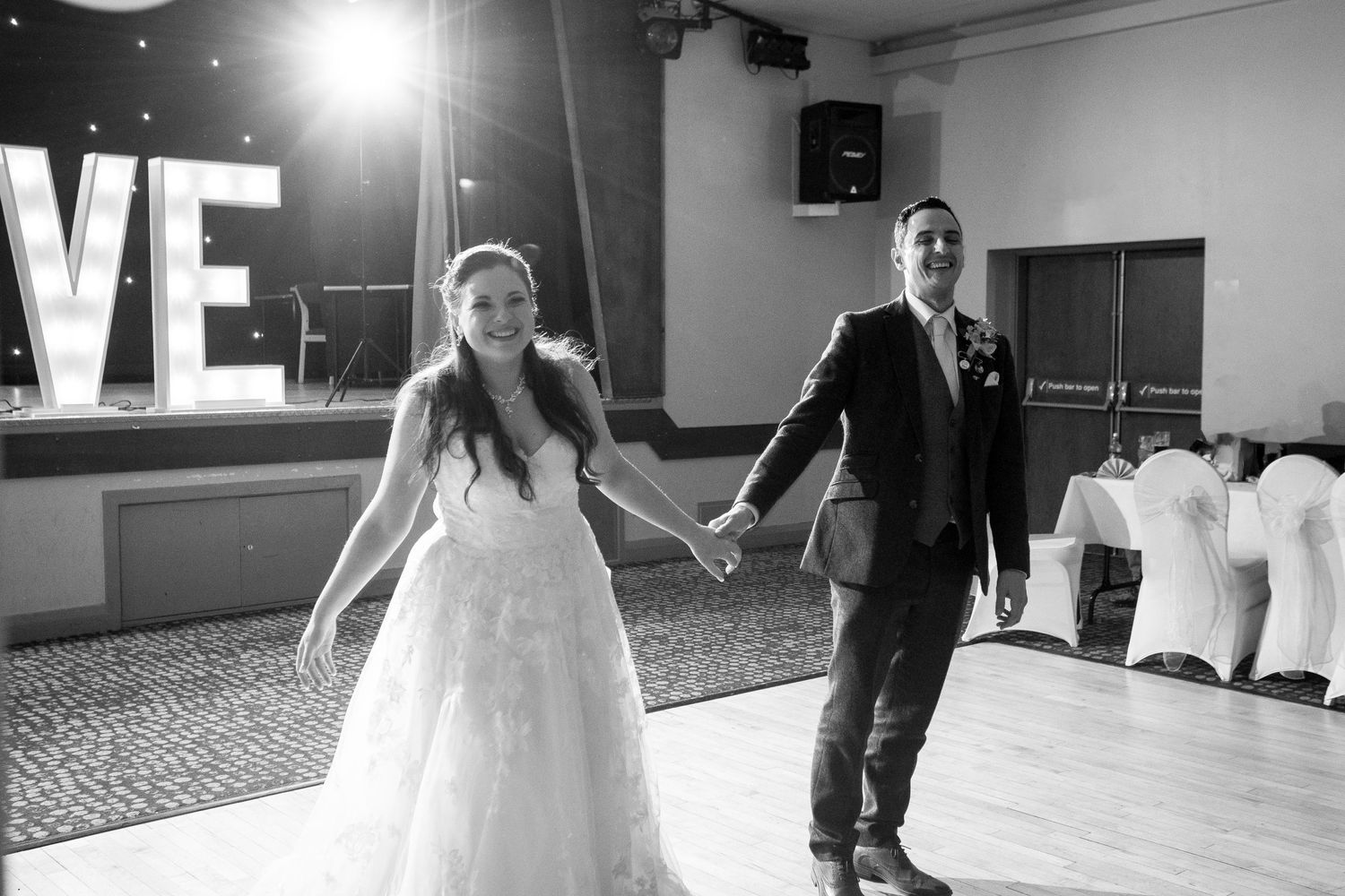 Couple holding hands while walking across dance floor at reception venue.
