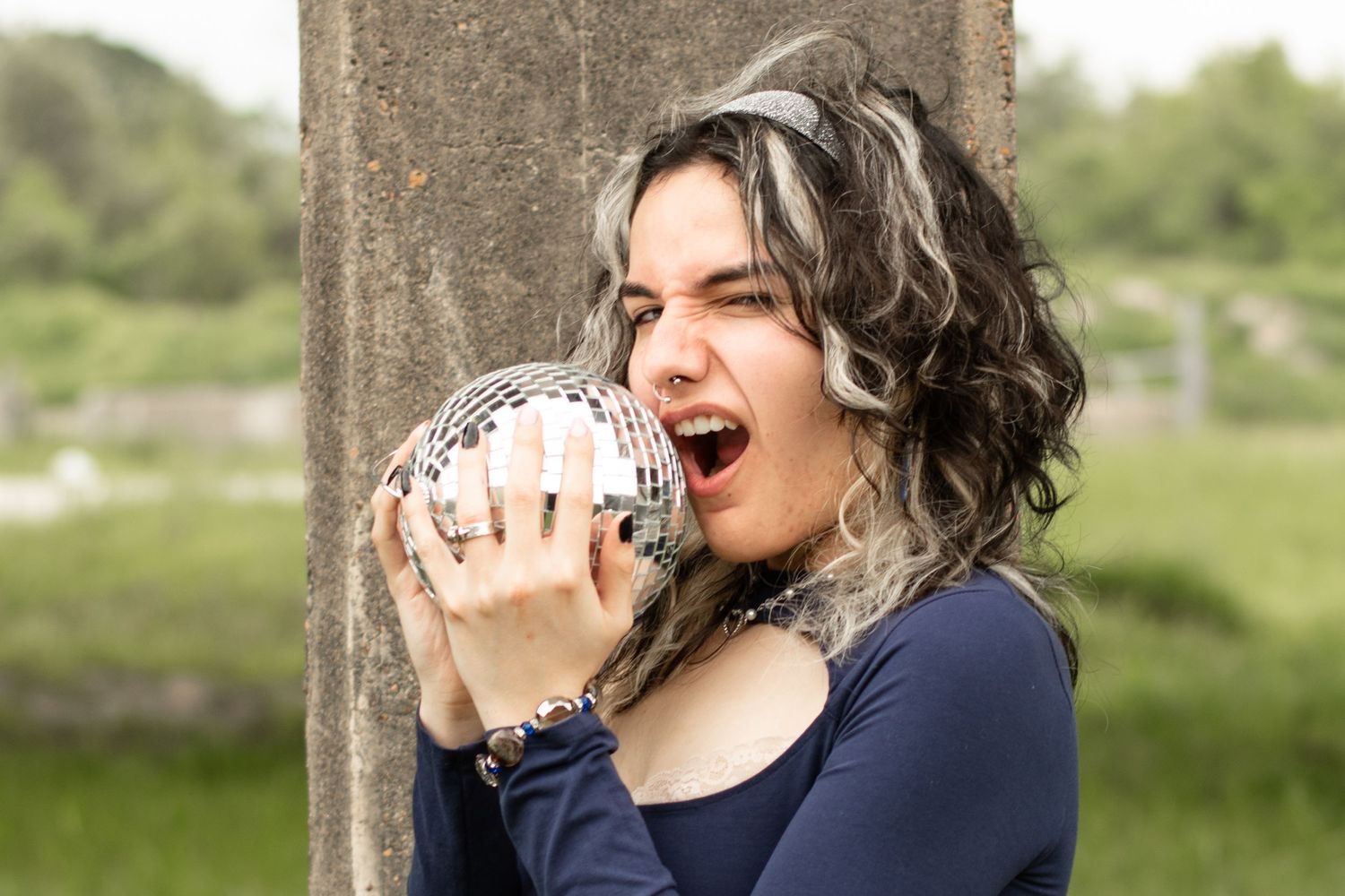 Person in navy top playfully poses with a disco ball outdoors.
