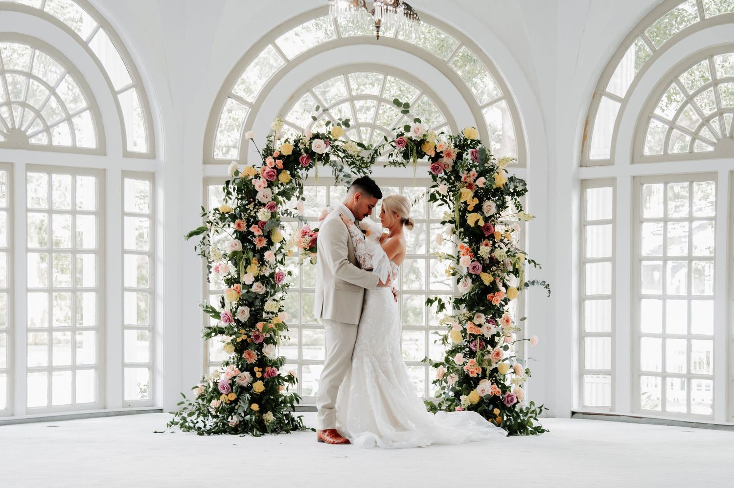 Bride and groom exchange vows at rustic indoor wedding ceremony with white chairs and floral arrangements.