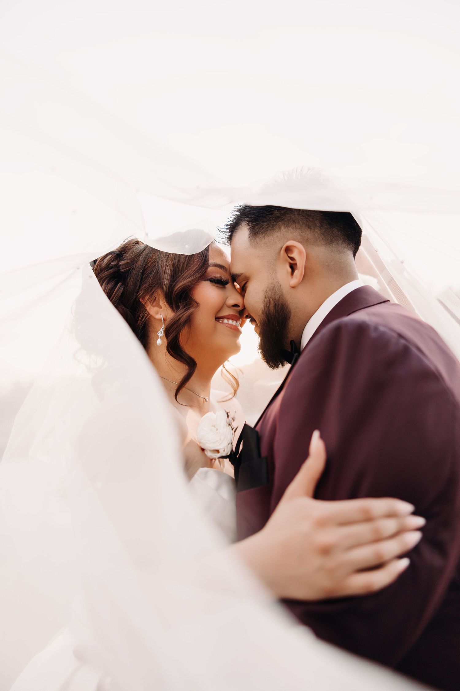 Intimate wedding portrait captured under flowing white veil.