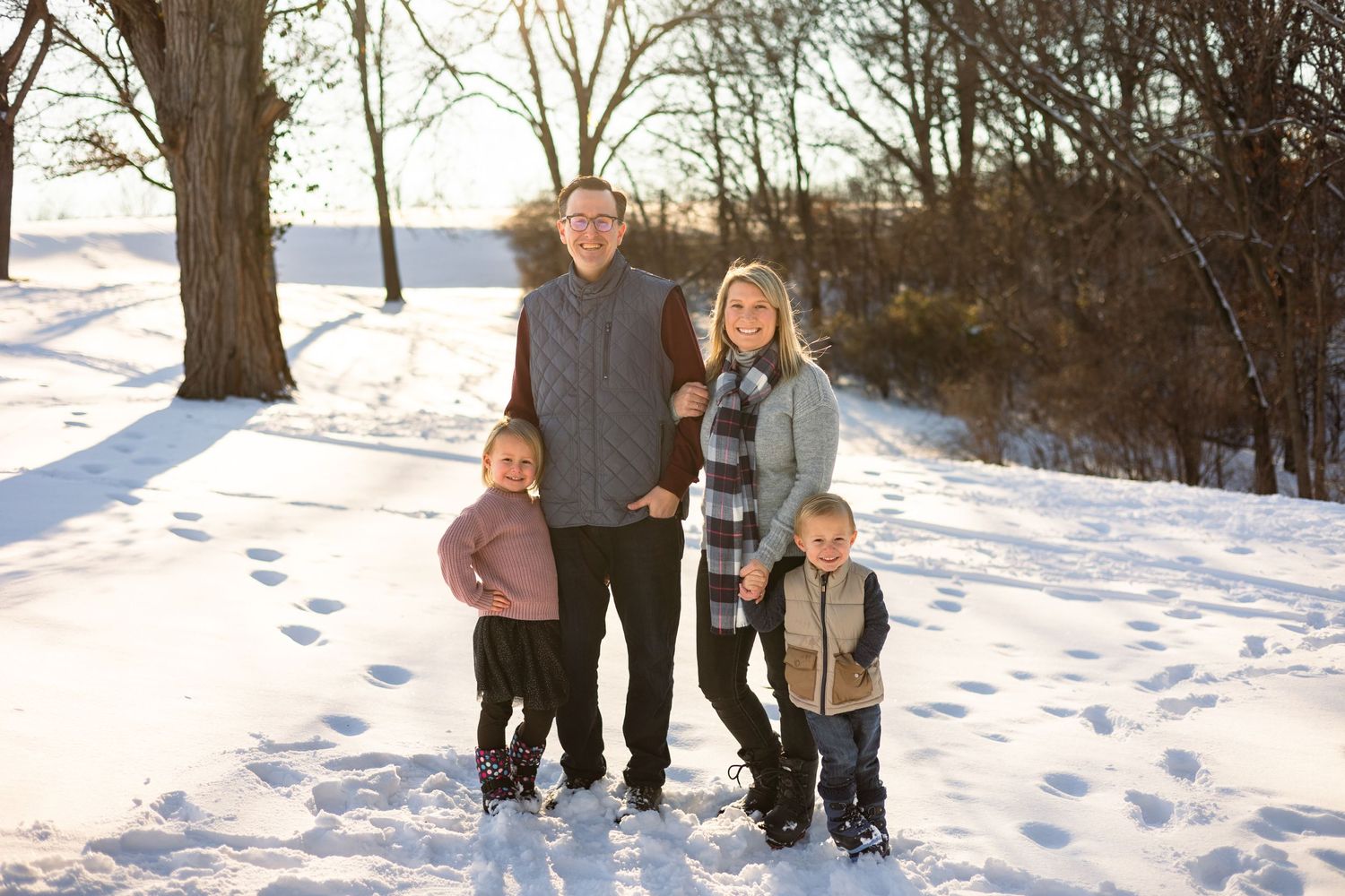 Family portrait session in snowy winter landscape with bare trees.