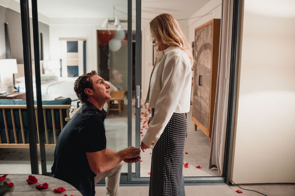 A romantic proposal scene with scattered rose petals and someone down on one knee.
