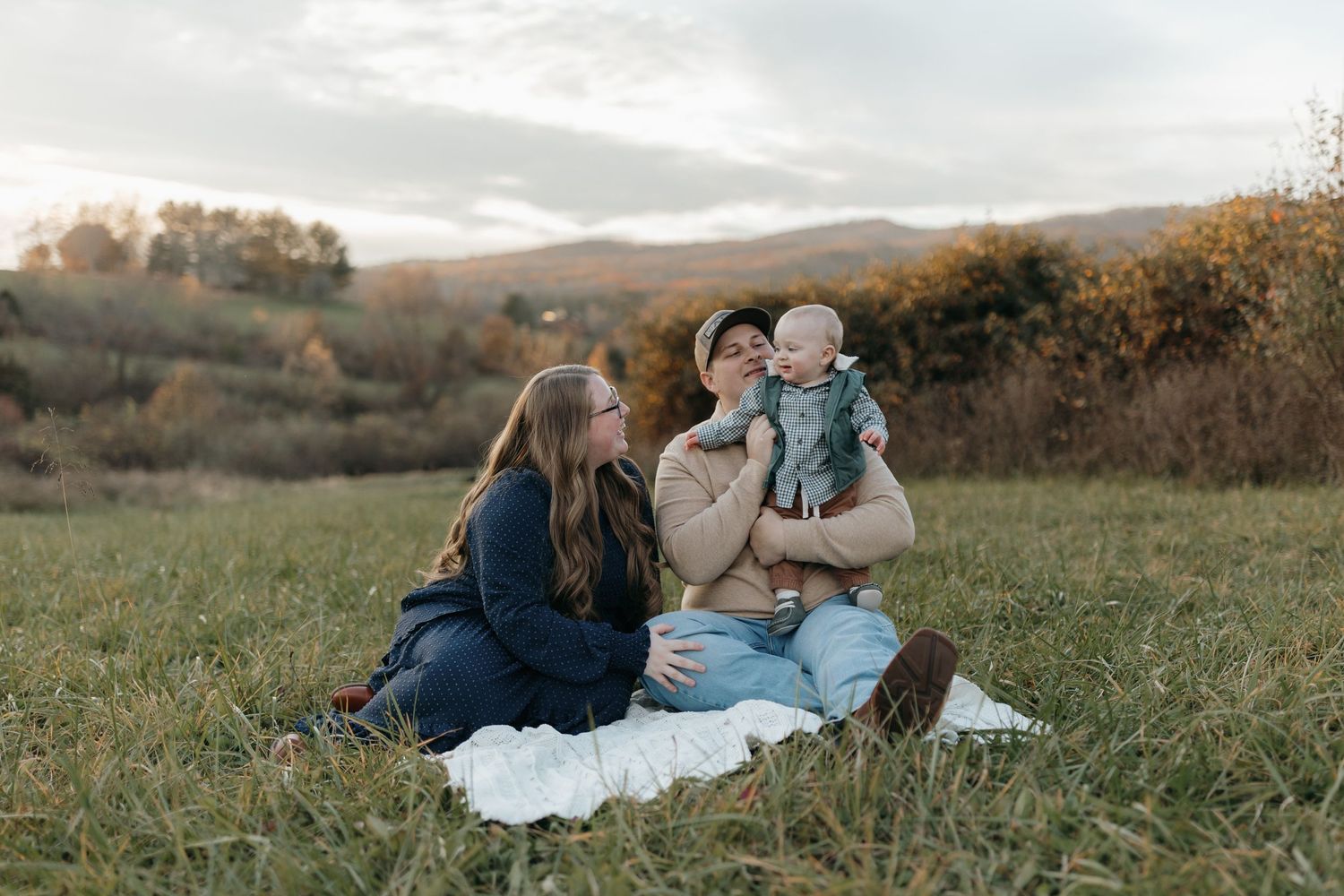 Family enjoys quality time together on a blanket in an autumn meadow with rolling hills in the background.