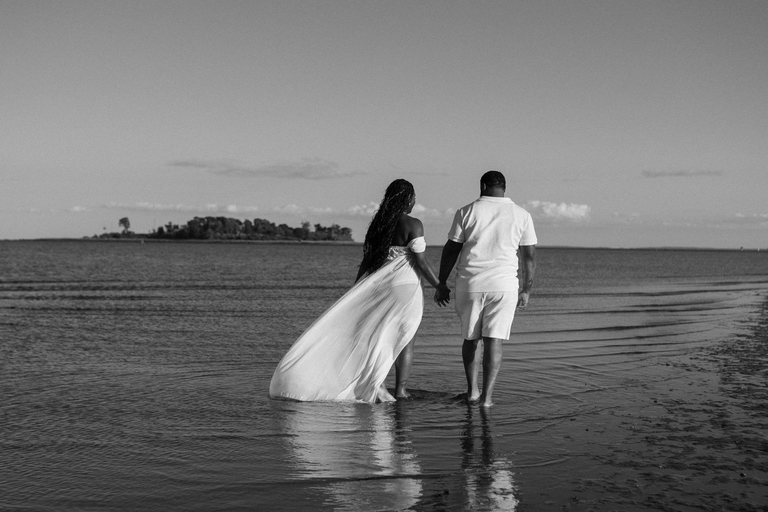 Black and white photo of couple walking along the beach at sunset.