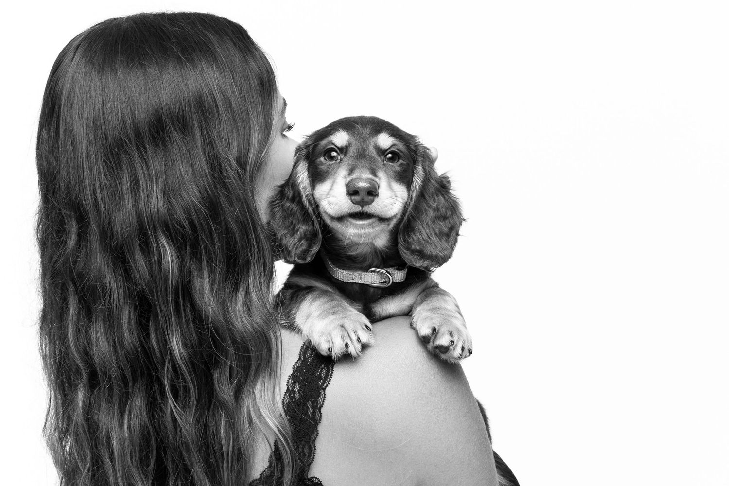 A person with long dark hair holds a sweet Dachshund dog against a white background in black and white portrait.