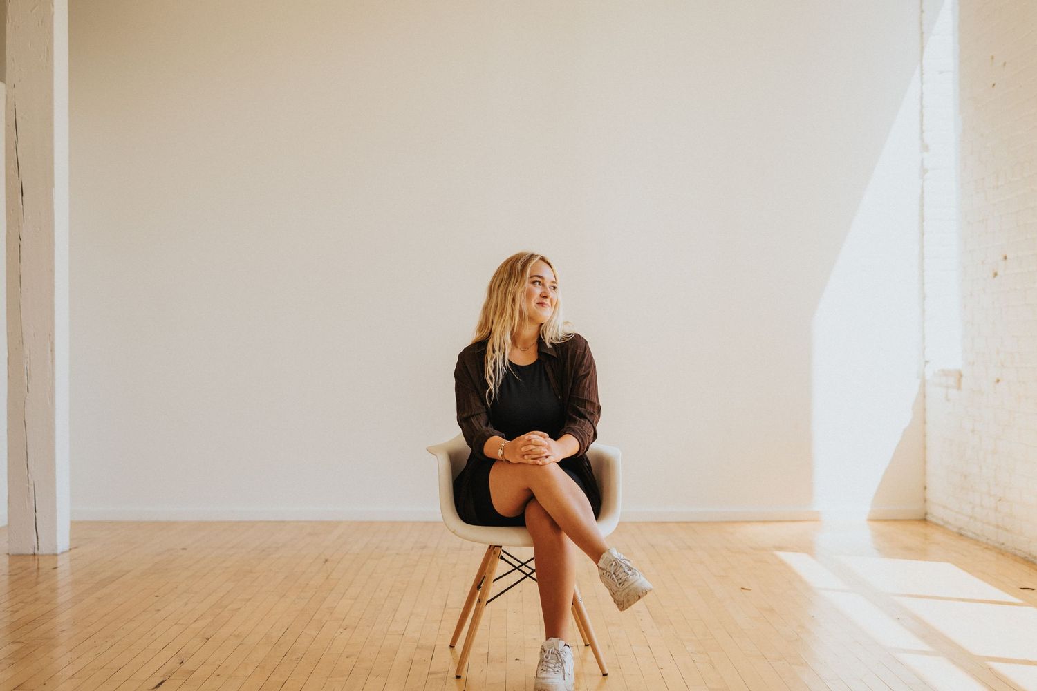 A person sitting cross-legged on a modern chair in a bright minimalist room with wooden floors.