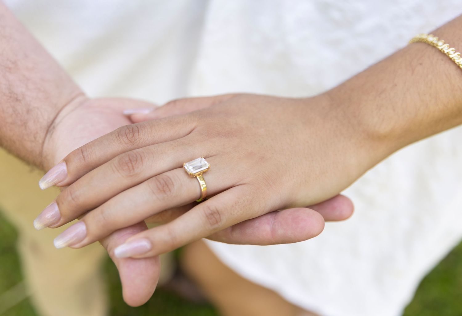 Two hands clasped together showing a sparkling engagement ring with a manicured light pink nail polish.