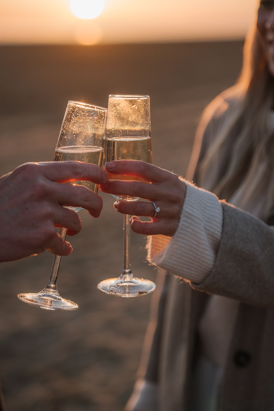 Two hands toasting wine glasses at sunset with golden sunlight creating a romantic silhouetted moment.