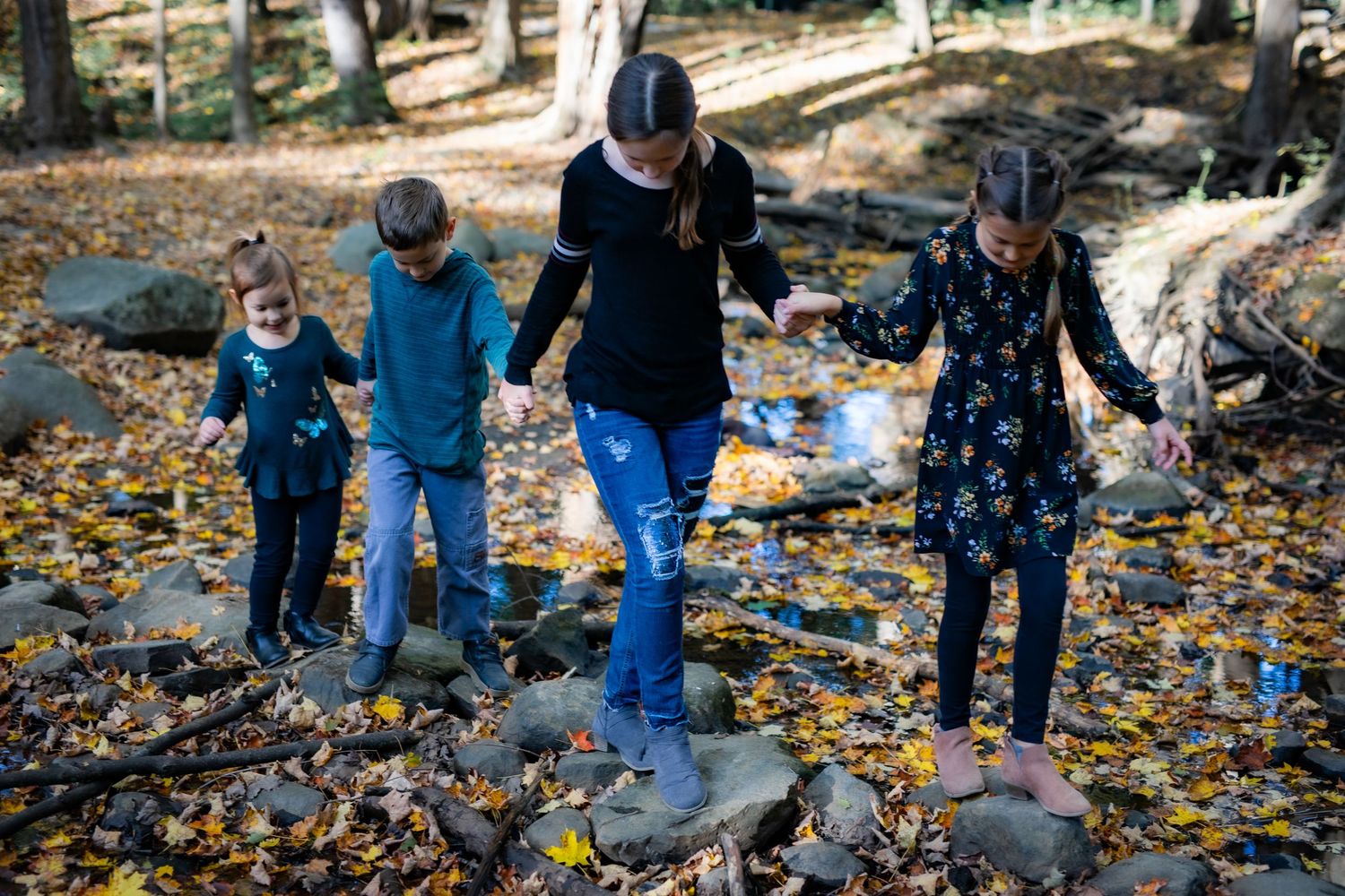 People walk together across rocks and fallen autumn leaves in an outdoor nature setting.