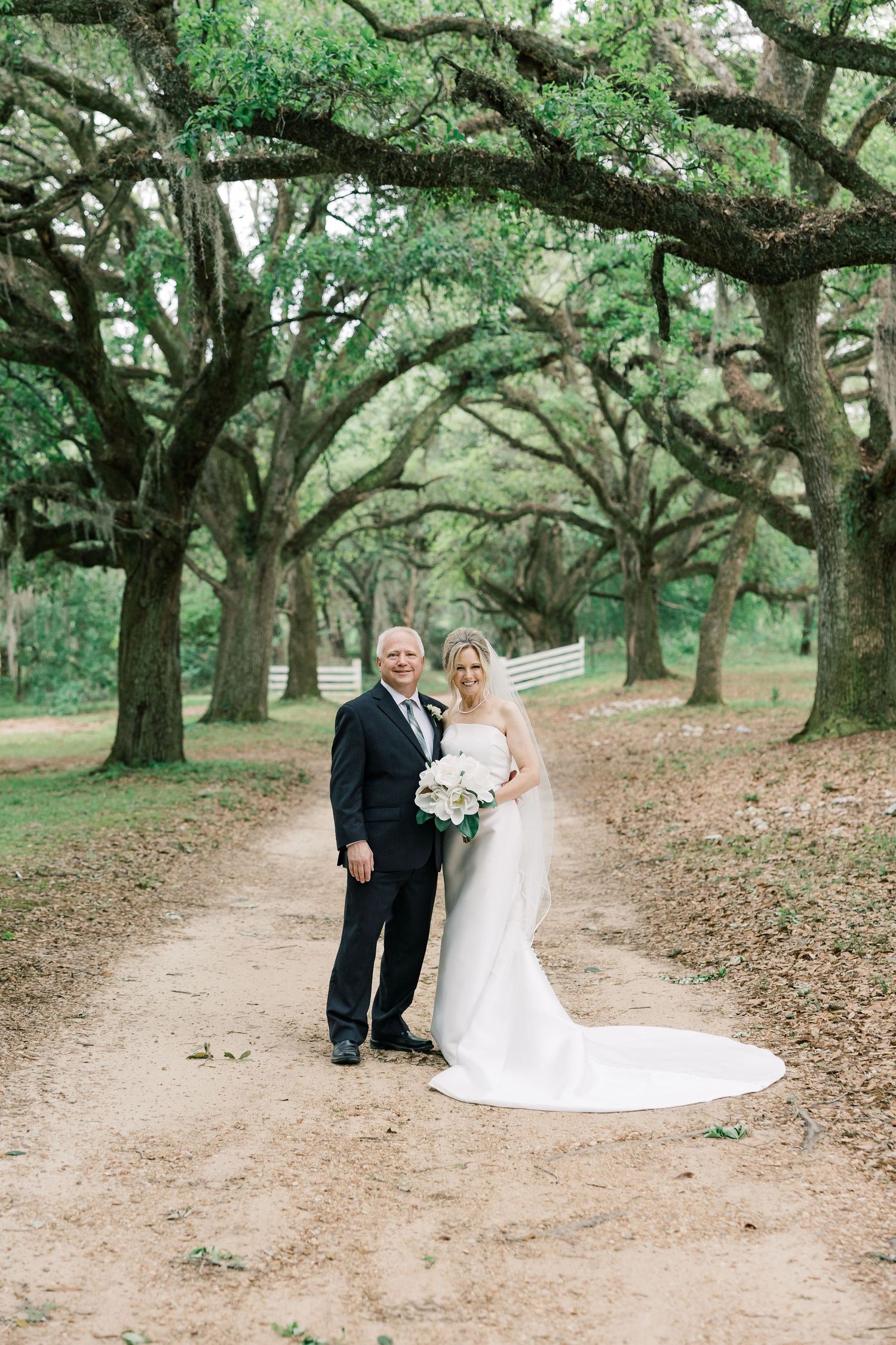 A couple poses along a picturesque dirt path under a canopy of majestic Spanish moss-draped oak trees.