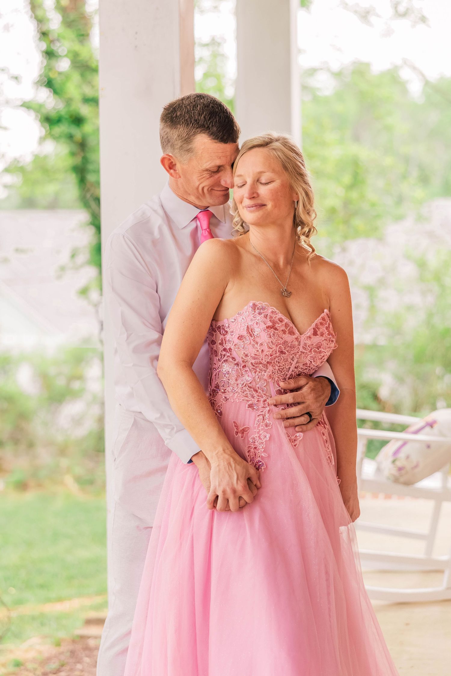 A couple shares an intimate moment on a white pillar porch in formal attire.