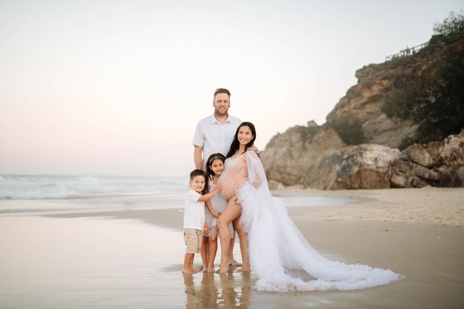 A family of four poses together on a scenic beach with cliffs in the background at sunset.