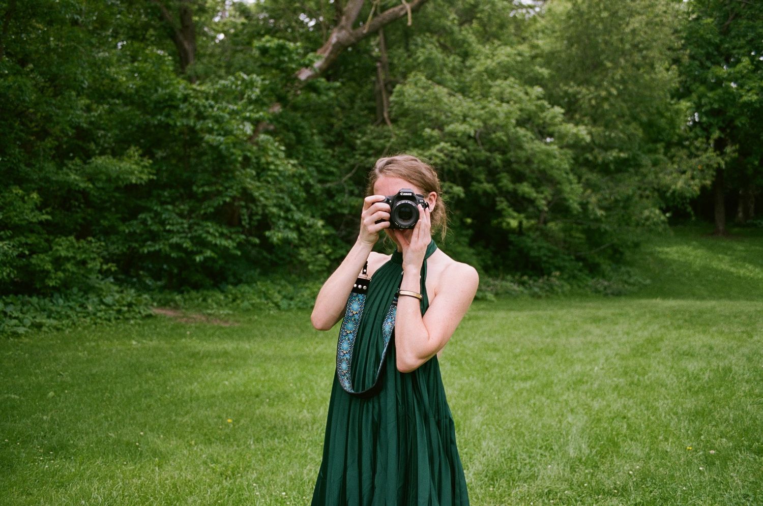 A photographer in a green dress takes pictures in a lush garden setting.