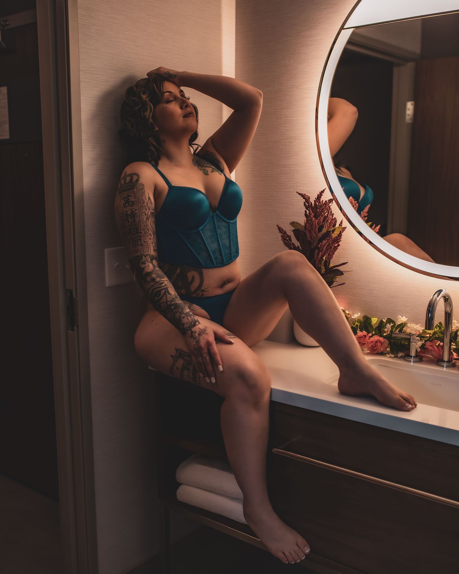 Boudoir photo in moody lighting featuring a teal lingerie set and intricate arm tattoos.