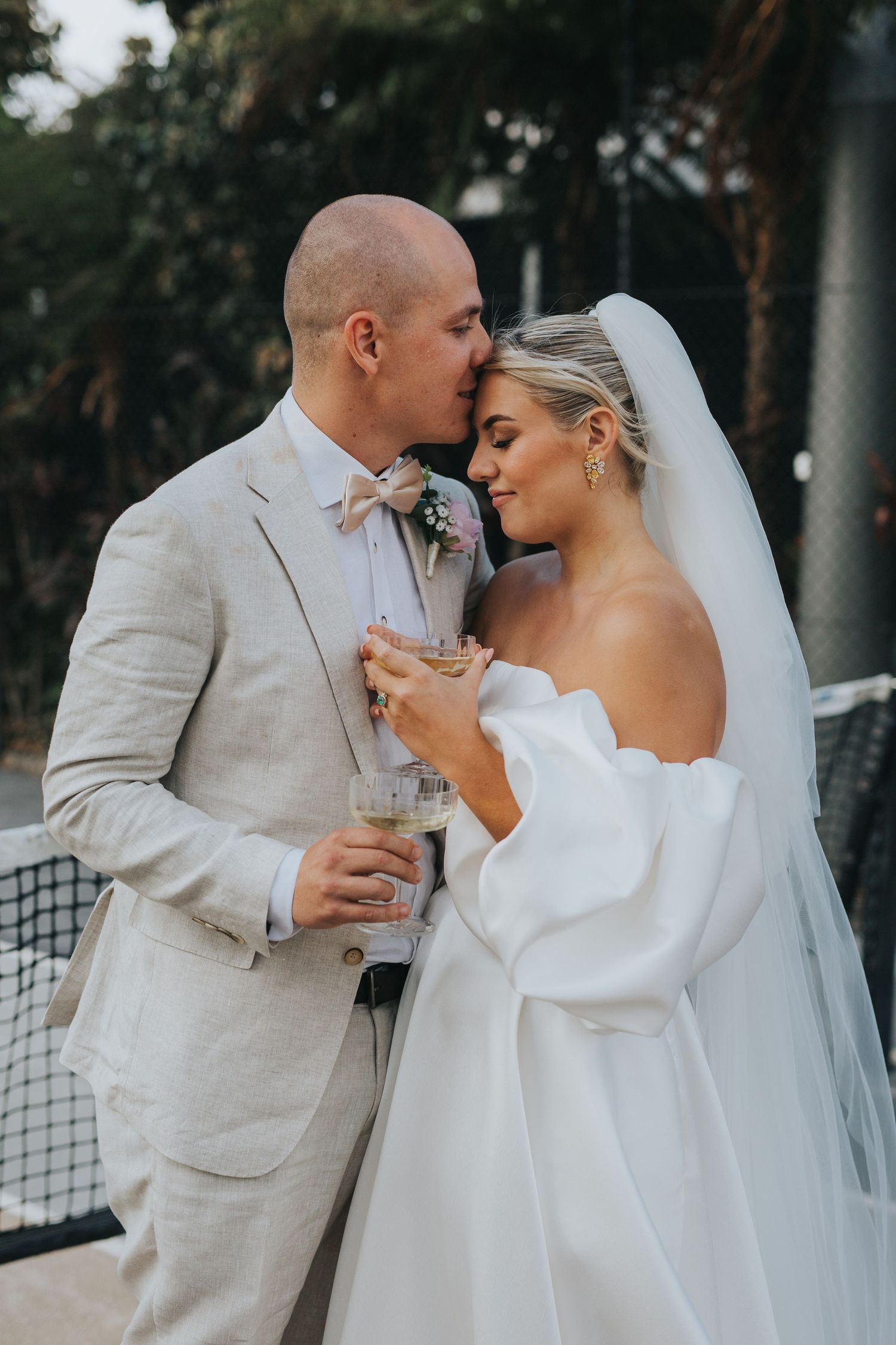 Newlywed couple shares intimate moment at outdoor wedding reception while holding champagne glasses.