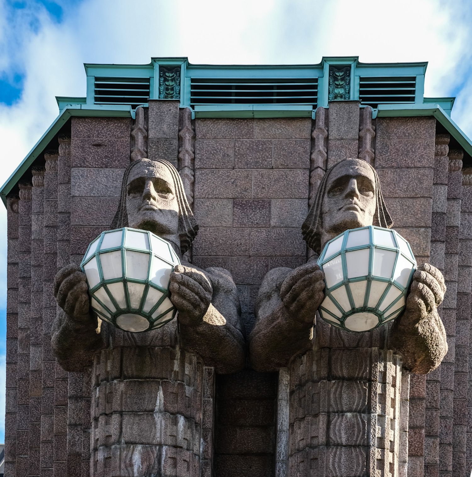 Two monumental granite statues holding glass globe lanterns flank the entrance of Helsinki Central Railway Station.