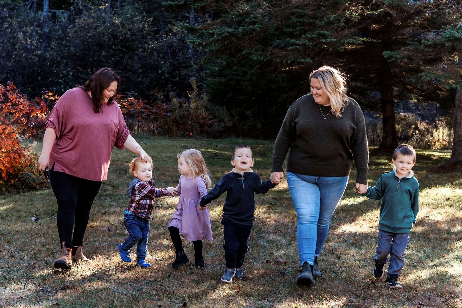 Annapolis Valley Nova Scotia family twin sisters of four smiling outdoors, with green trees behind.