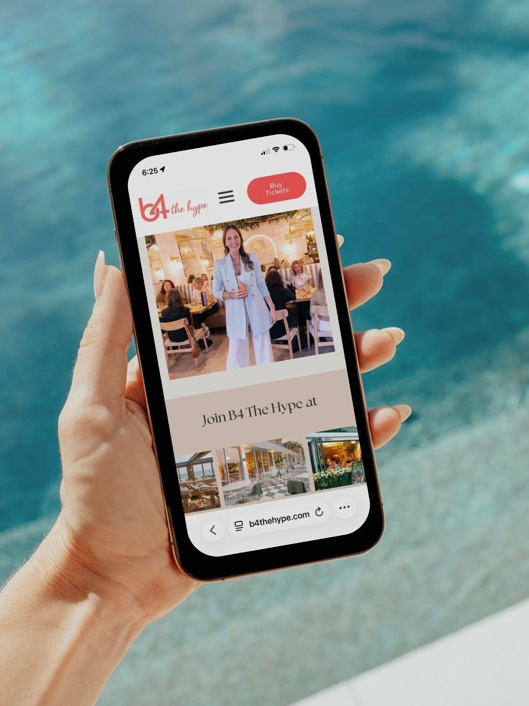 Hand holding smartphone displaying B4 The Hype website near a pool, showing a woman in white outfit on homepage.