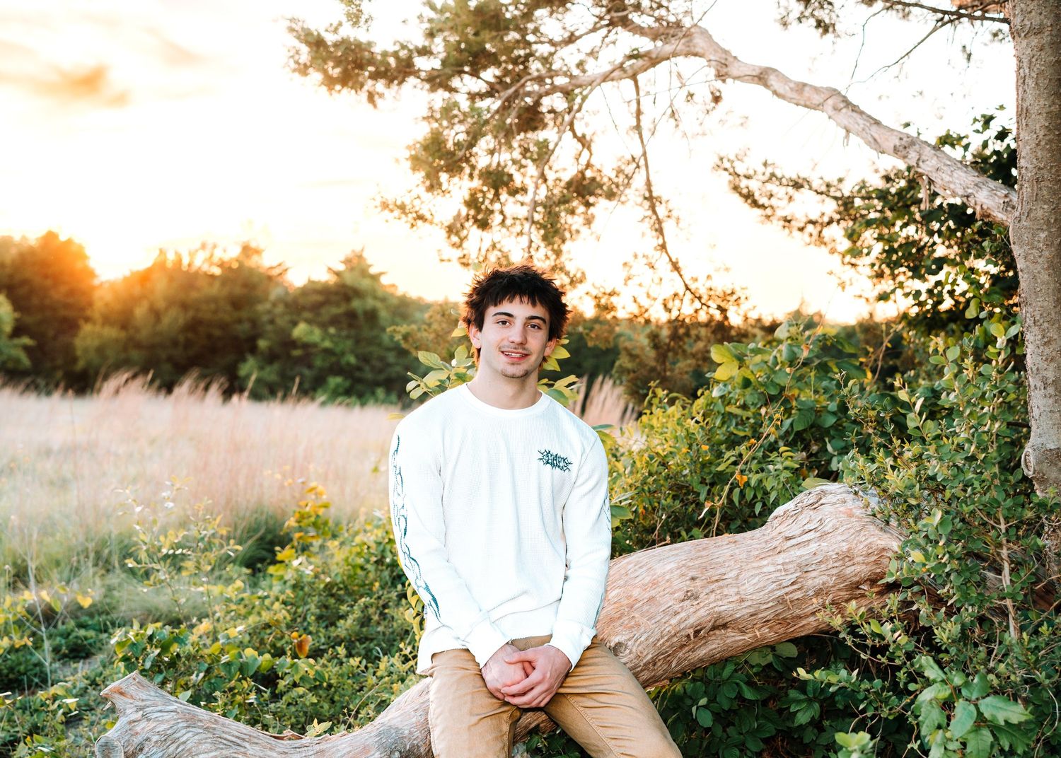 Young man in navy sweater and white pants standing on stone path by a pond near a historic building.