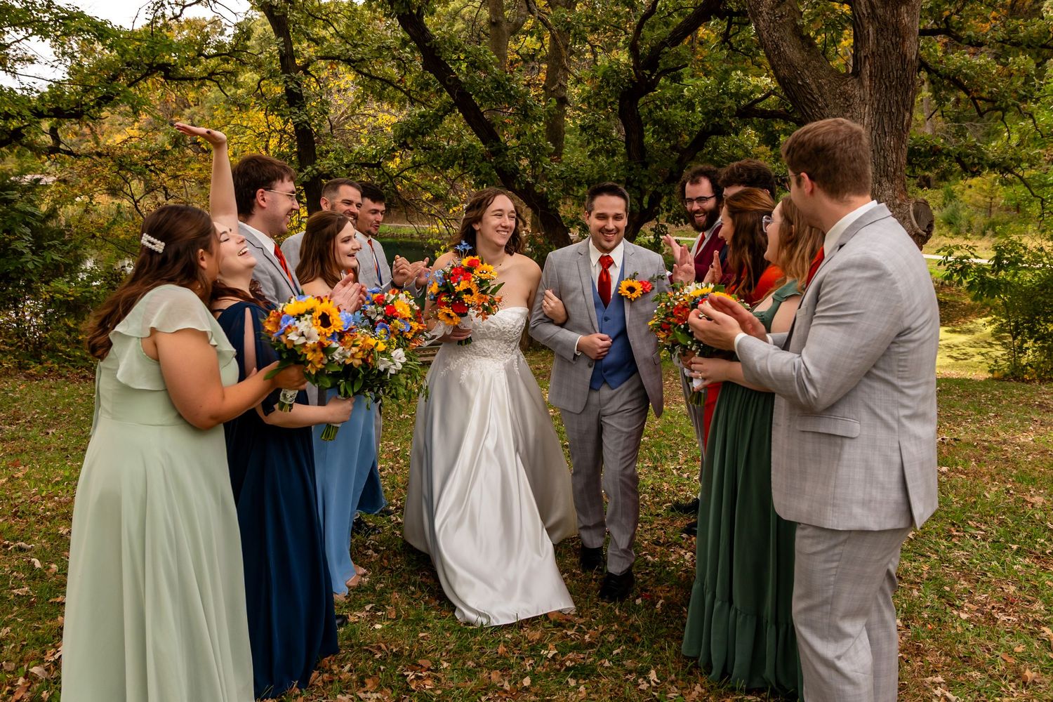 Wedding party celebrating outdoors in autumn, bridesmaids in sage and navy with colorful bouquets at Platte River State Park in Louisville