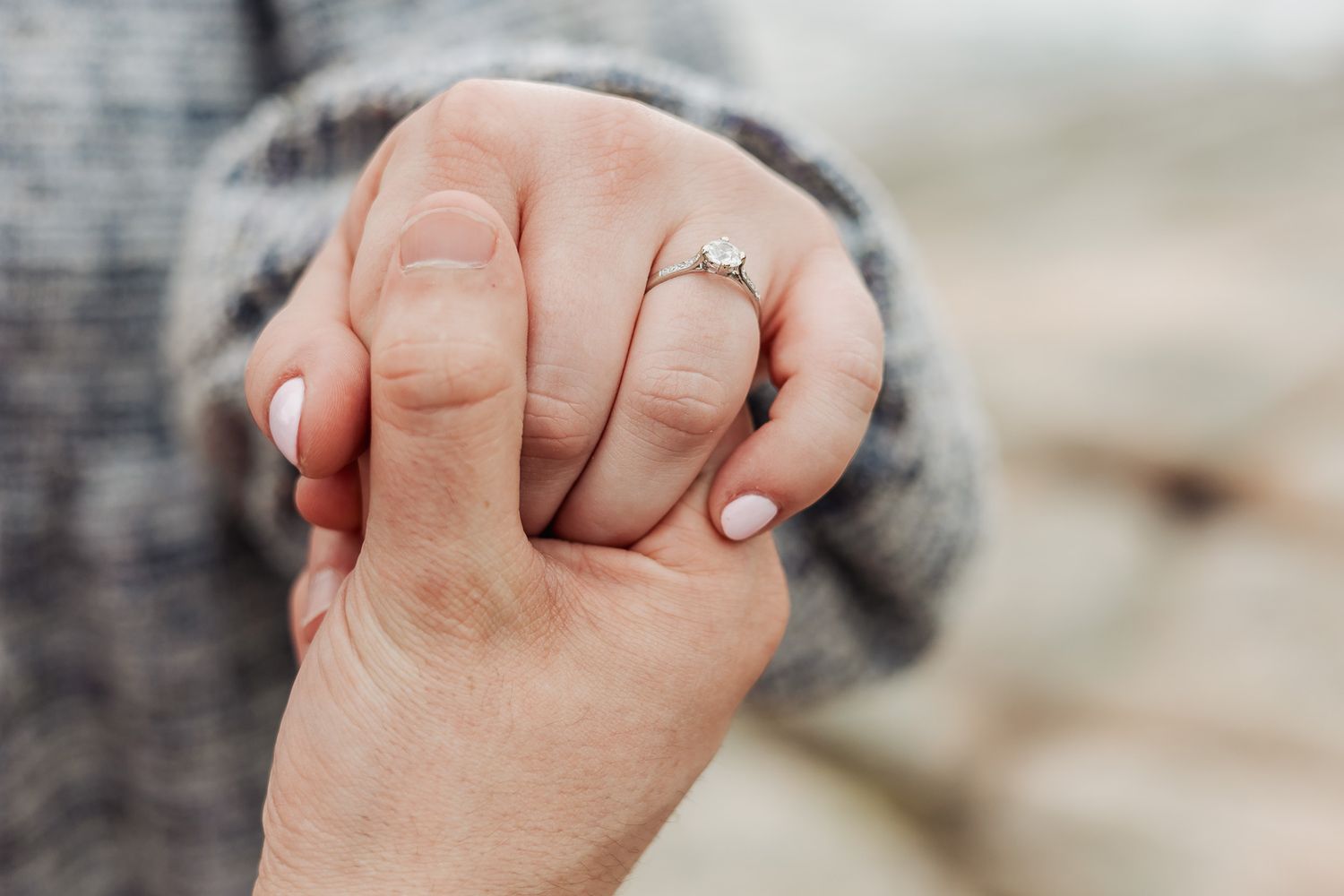 Close-up of two hands holding, one wearing a diamond engagement ring on the ring finger.