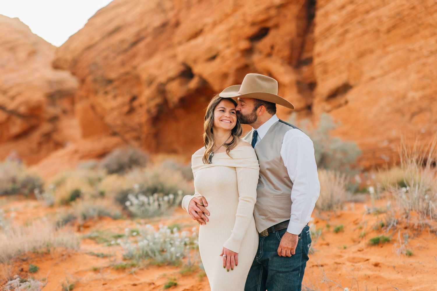 A couple stands between red sandstone formations at Valley of Fire State Park surrounded by desert brush and sage.