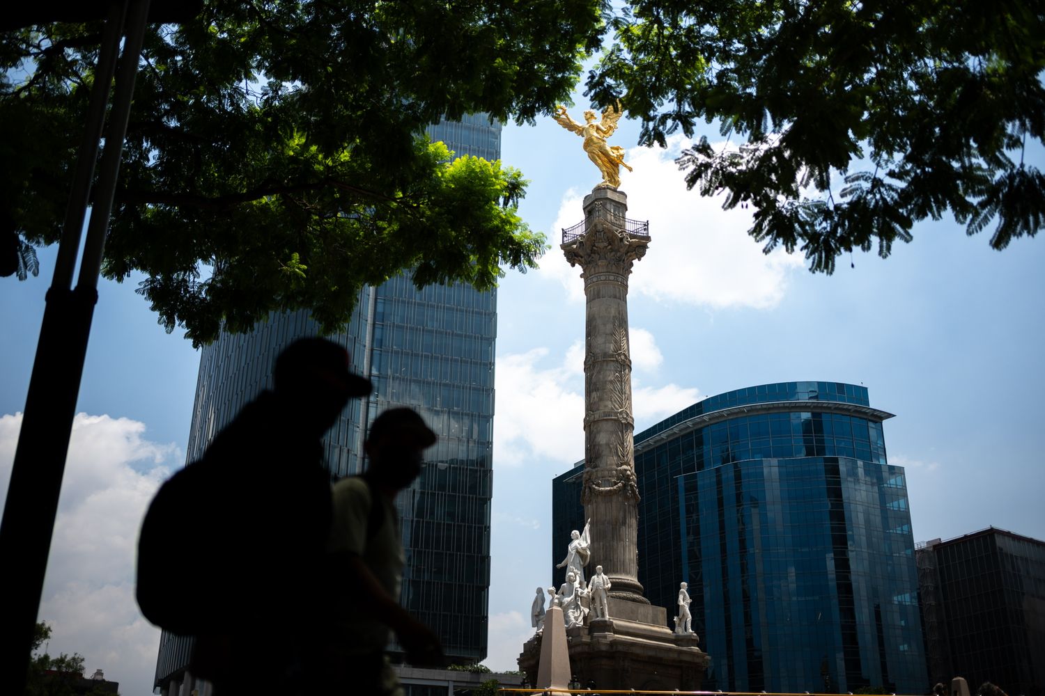Angel of Independence monument in Mexico City with golden statue atop column, framed by trees and modern skyscrapers.