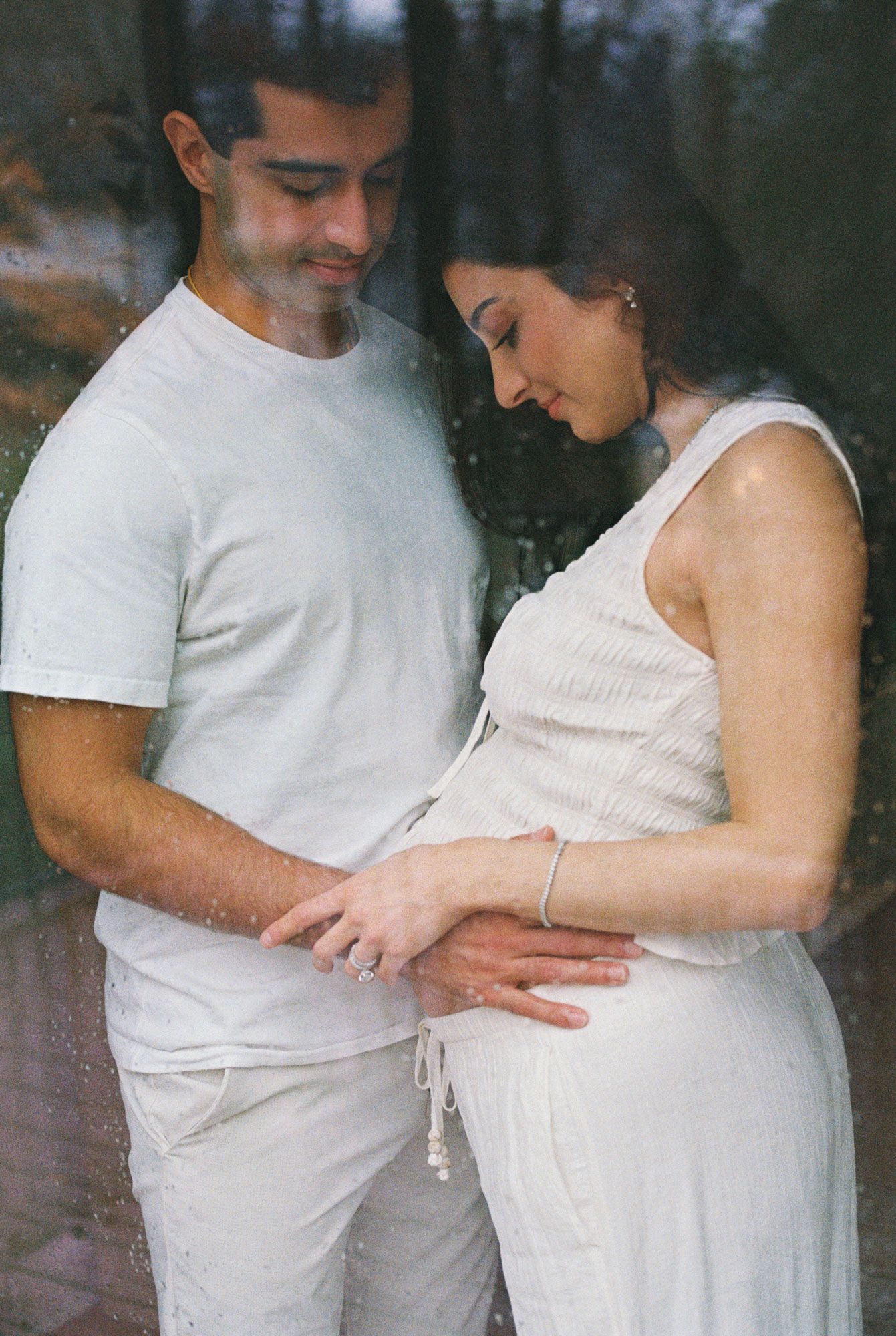 A series of intimate maternity photos showing a couple in white clothing lying together on a light gray carpet.