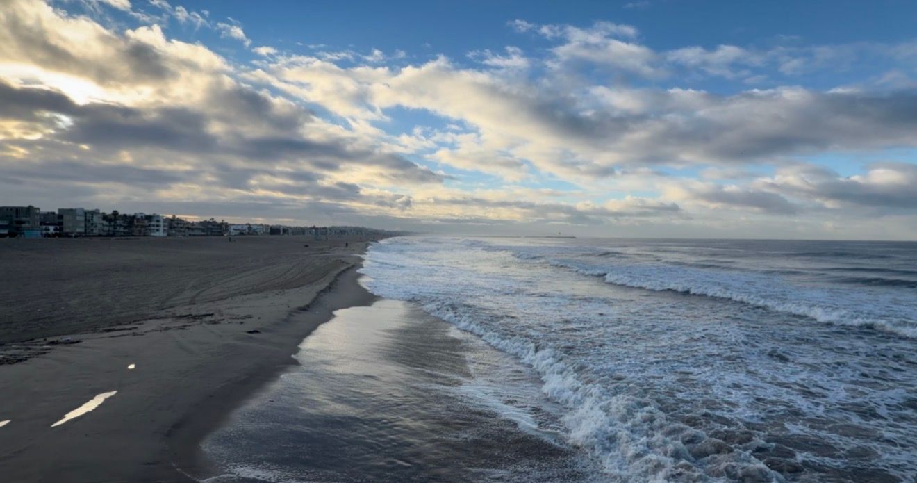 Panoramic beach landscape with dramatic clouds and rolling waves crashing along the shoreline at sunset.