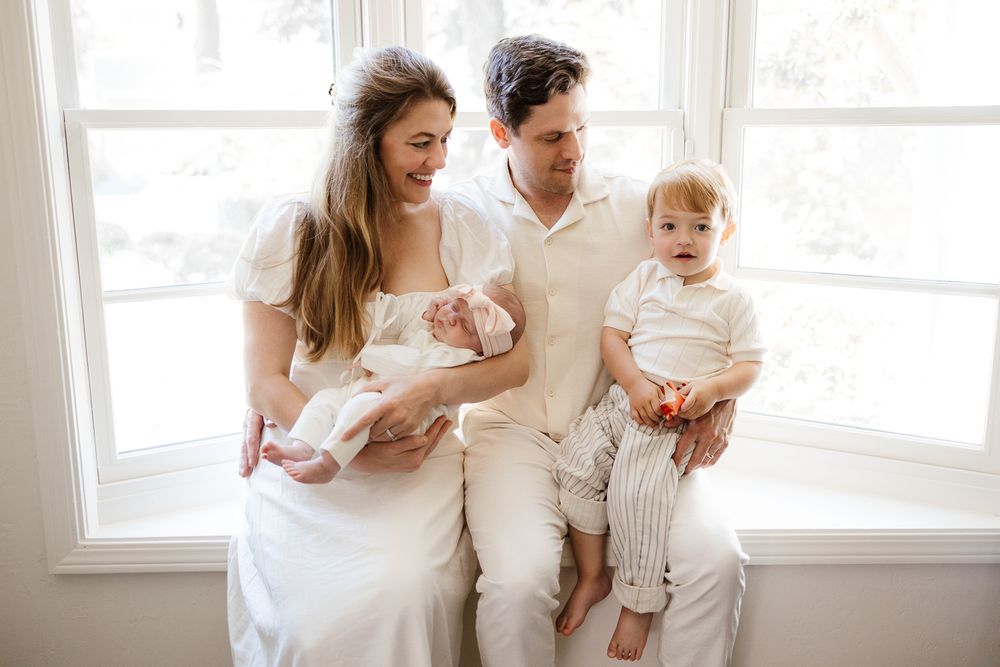 Parents hold their newborn baby and toddler son in a family portrait in their home in Palo Alto