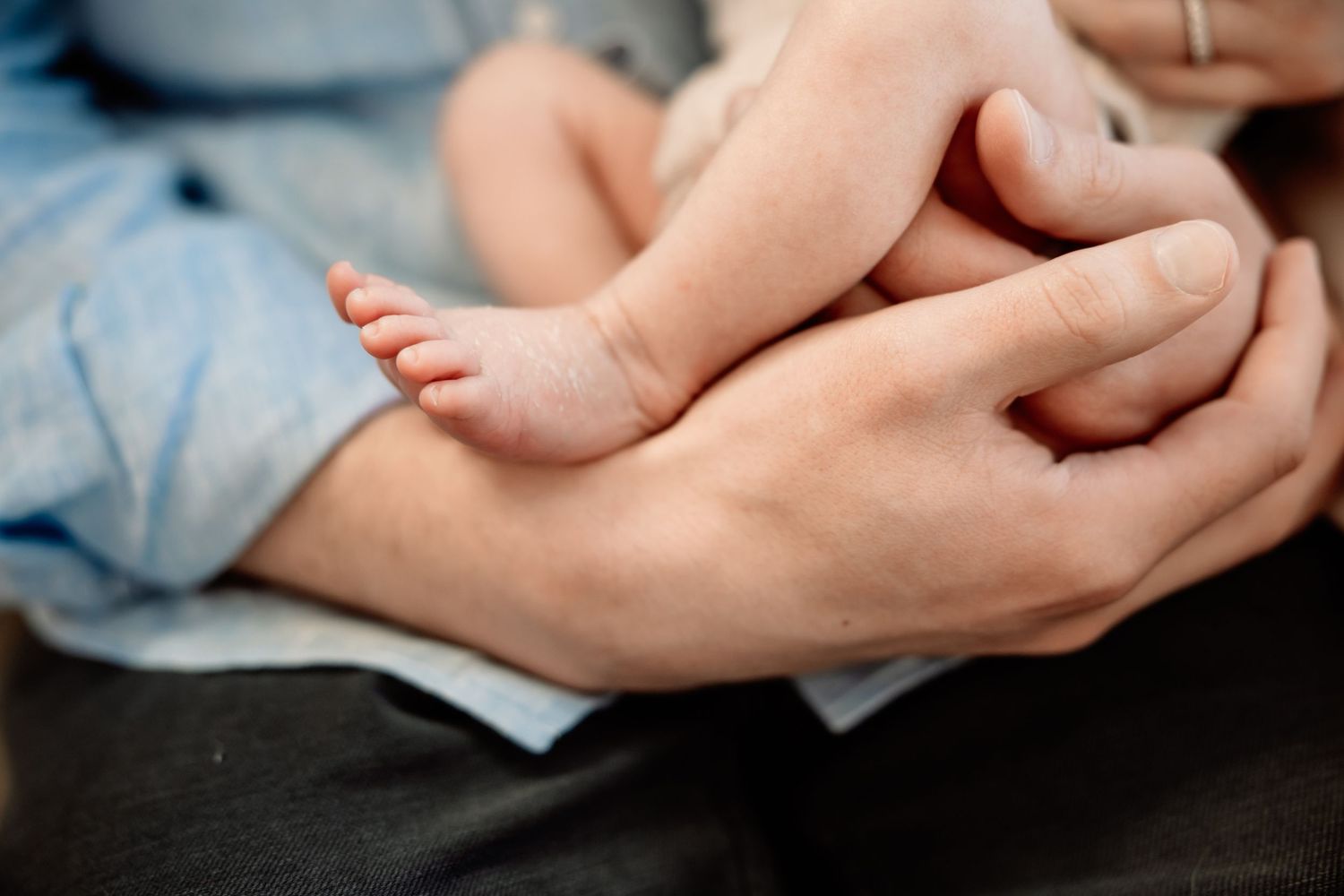 Close-up of adult hands gently cradling tiny newborn baby feet, symbolizing love and parental care.
