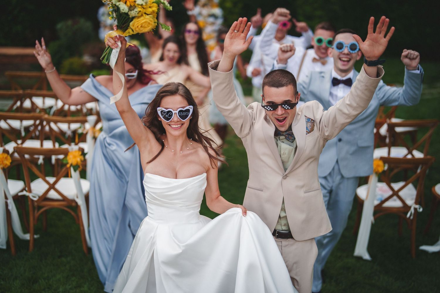 Joyful wedding guests and newlyweds celebrate with raised arms during an outdoor reception ceremony.