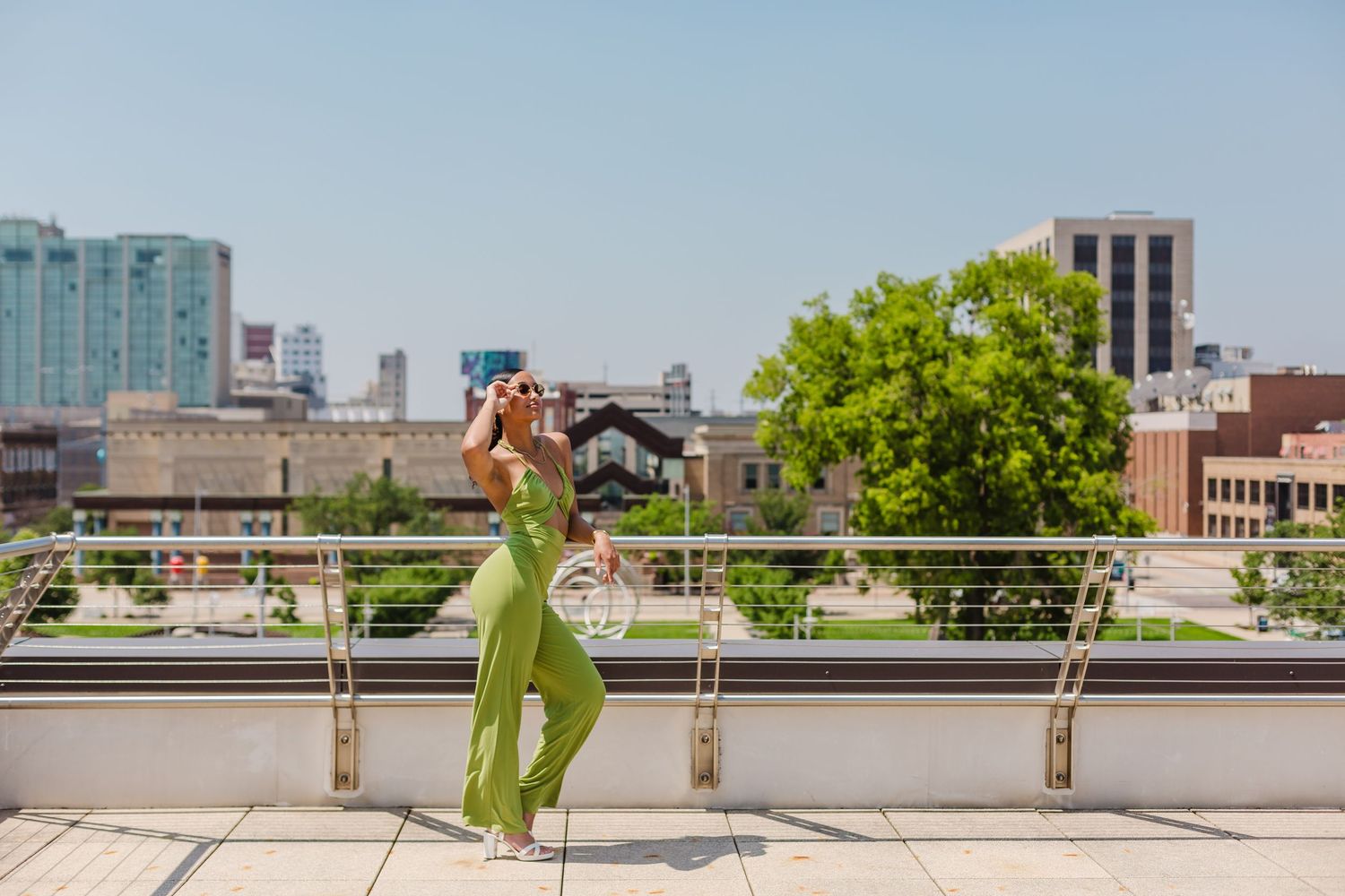 A green jumpsuit-clad figure poses for five photos on an urban rooftop with city buildings in the background.